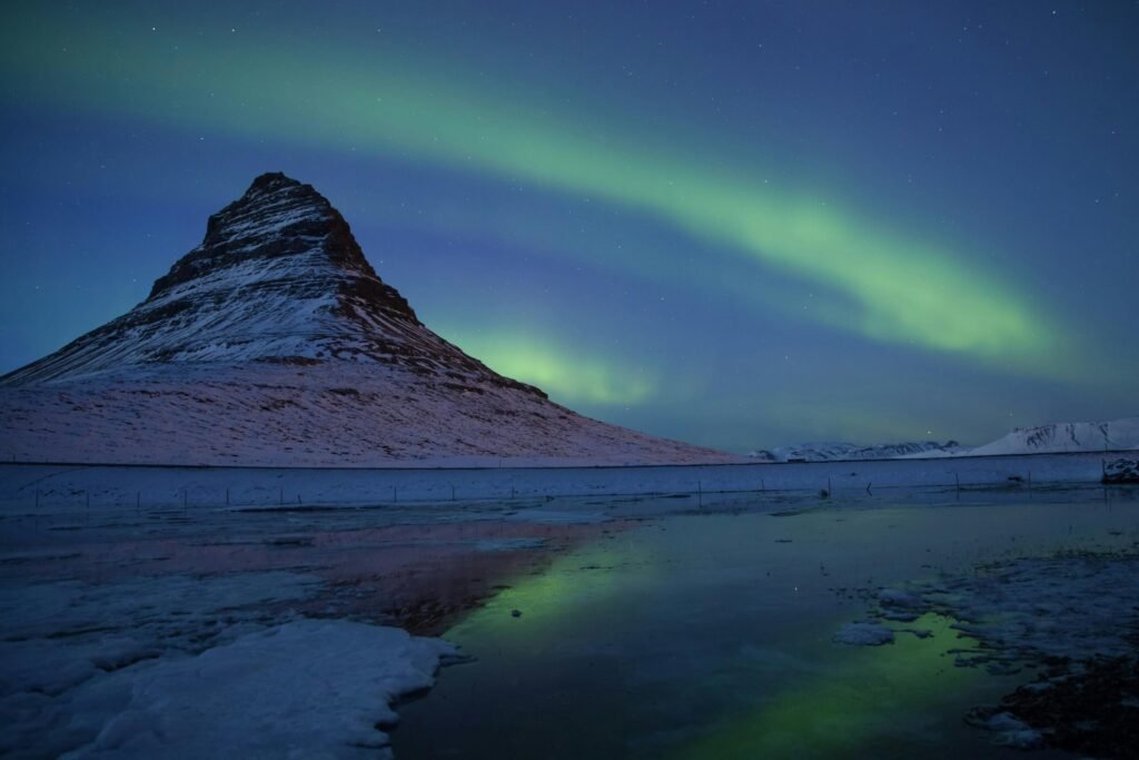 Stunning Northern Lights over Kirkjufell mountain reflected in icy lake, Iceland