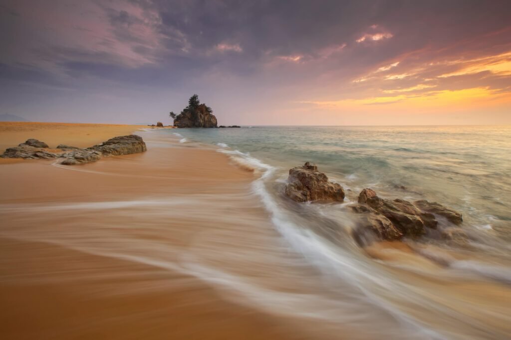 Tranquil beach scene at sunrise with soft waves and rock formations.