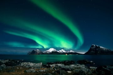 Breathtaking northern lights display over snow-covered mountains and serene waters in Lofoten, Norway.